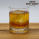 Root Shoot Maltings High Rye Bourbon Whiskey in a glass with ice on a wood table with Root Shoot Malting Logo in the upper right corner.