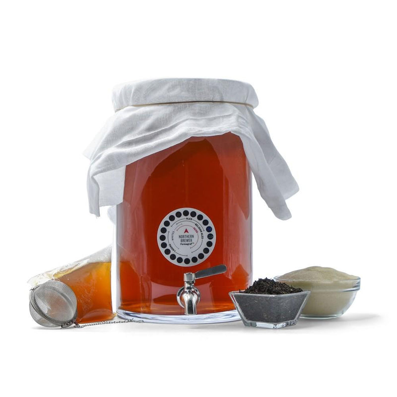 Kombucha fermenting with adhesive thermometer, stainless steel spigot, ingredients, stainless steel tea ball, and SCOBY packaging